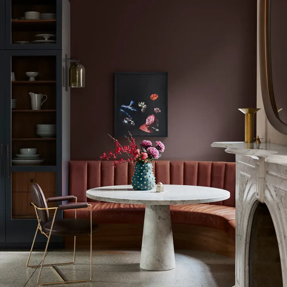 Dining area with marble table and cushioned seating. Shelving and fireplace feature to either side.