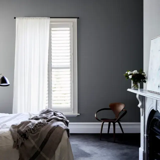 Bedroom with bed off edge of image, lamp in corner and chair in opposite corner with an old fireplace and painting above it. 
