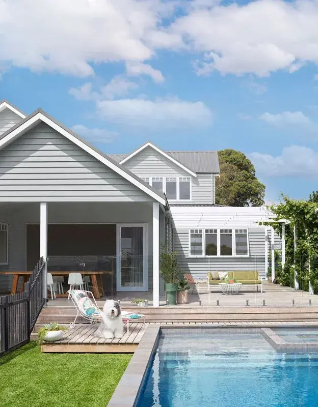 Exterior of house with pool and dog sitting on deck by the pool next to a pool lounger chair
