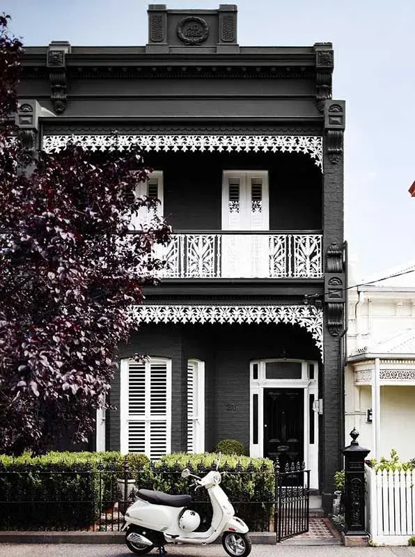 Black double-storey brick terrace house with white iron lace and black door.