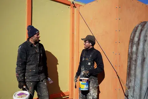 Two men standing outside Hillary's Hut holding cans of Dulux paint