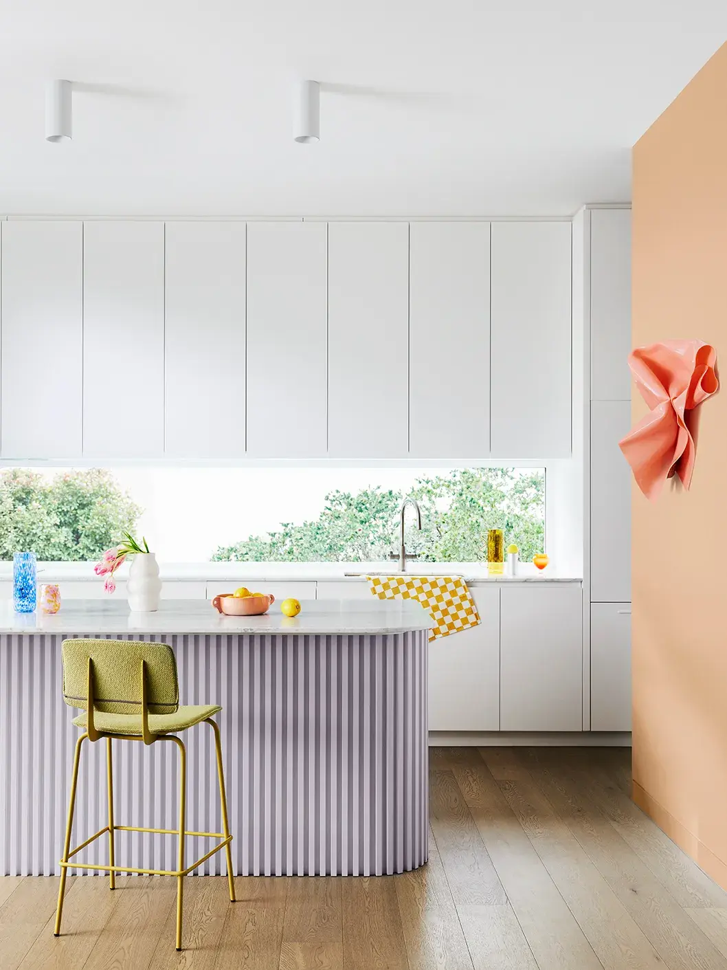 Spacious kitchen with white cabinetery, lilac island bench and orange feature wall