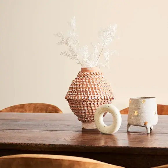 Wooden table in neutral room with beige vase, pot and decor.
