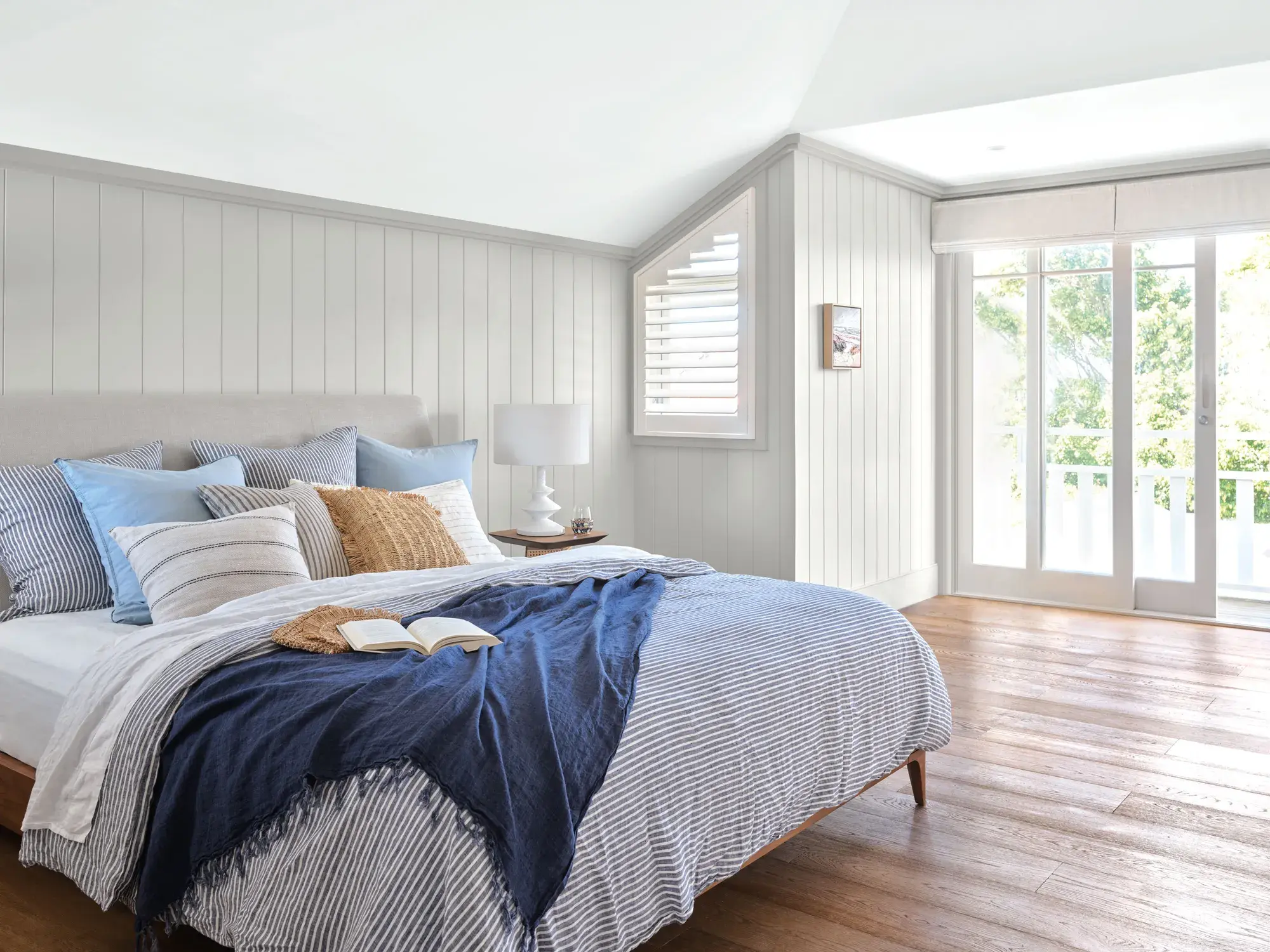 Green and white bedroom with sliding white framed exterior glass door, bed with blue linens