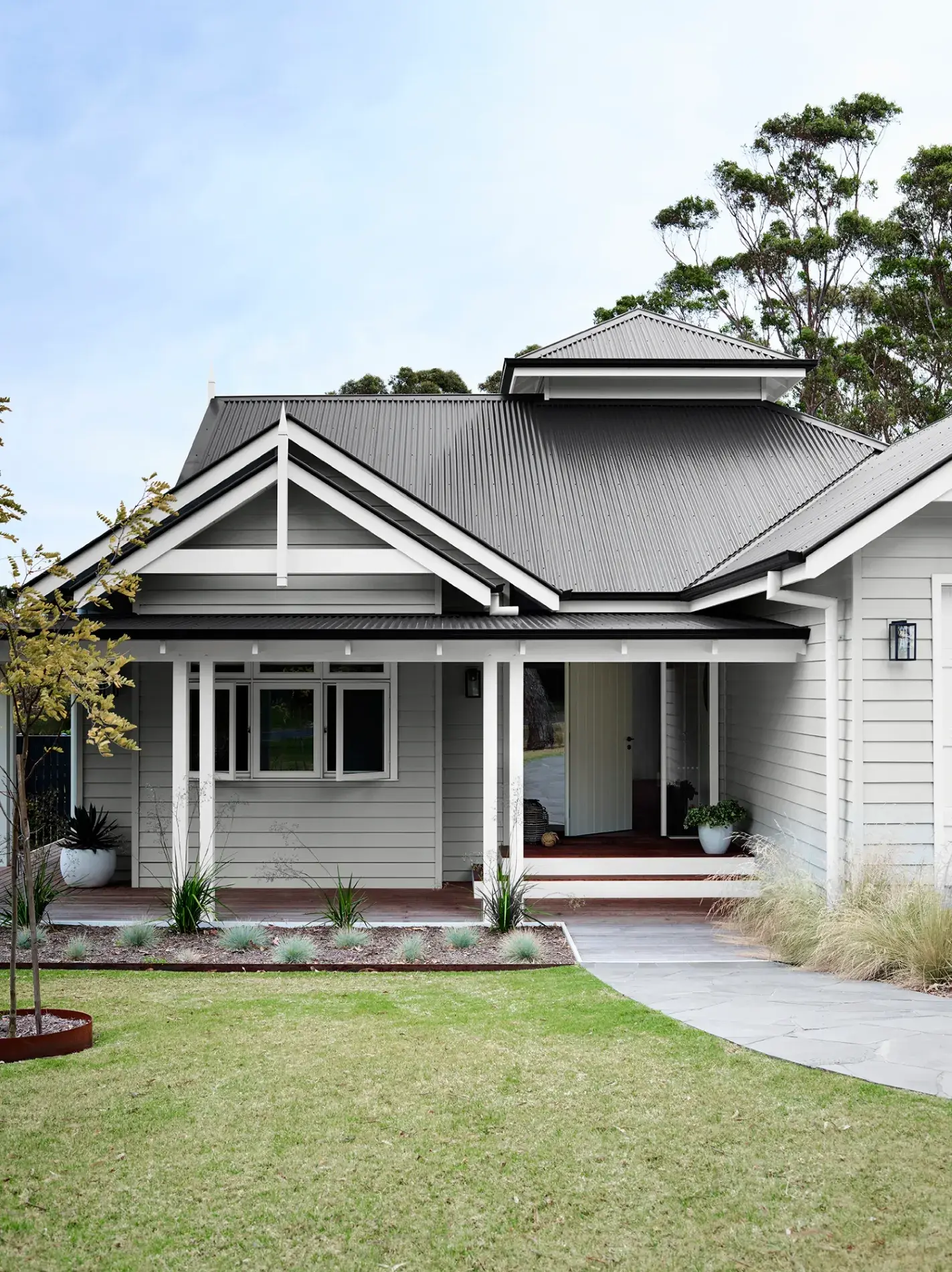 Dulux Colorbond® -  exterior grey weatherboard house with white pillars and a concrete path leading to the front door. Grass alongside the pathway and a front lawn. 