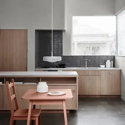 Kitchen with small peach table, wooden cabinetry and stone benchtops. Low hanging light above bench.