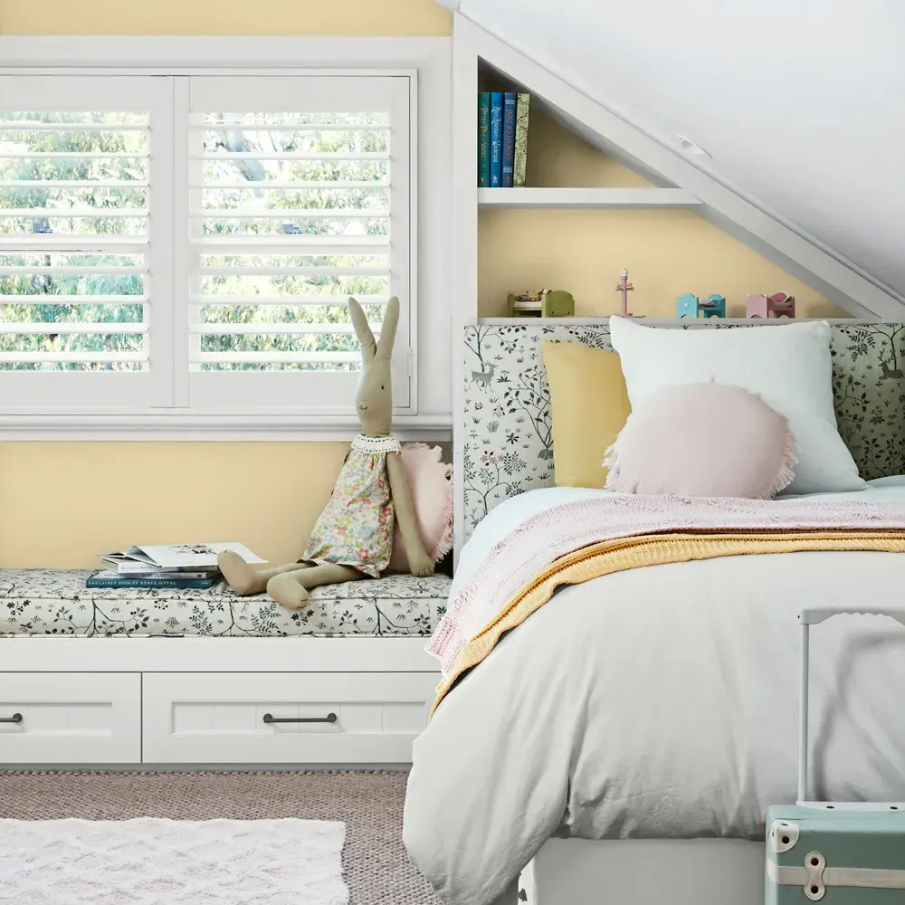 Yellow kids bedroom with bed, book shelf behind and various toys and decorative items.
