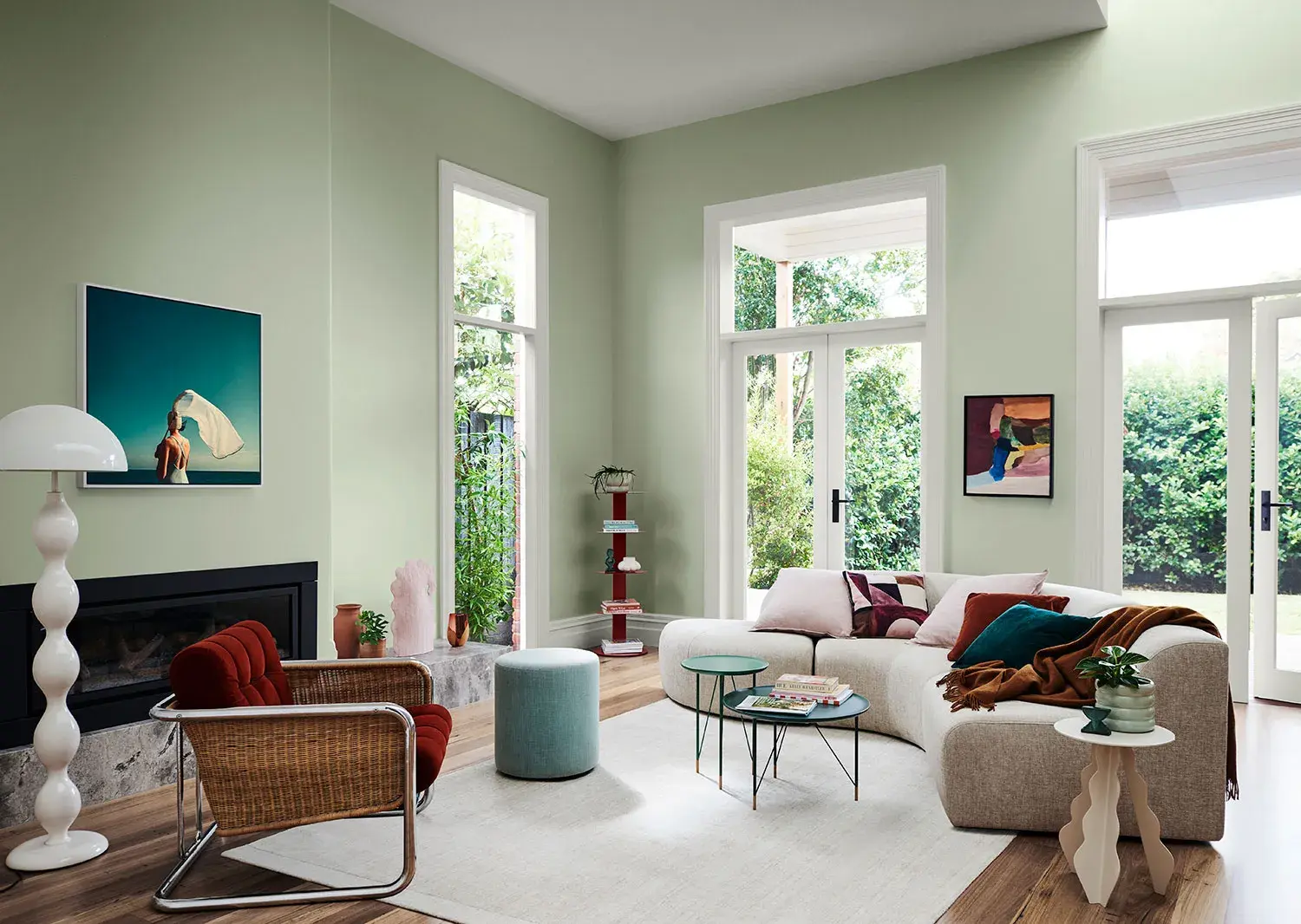 A scandi style living room with a curved couch and a chair. There is a gas fireplace with a photo hanging above it on the wall and the walls are painted light green.