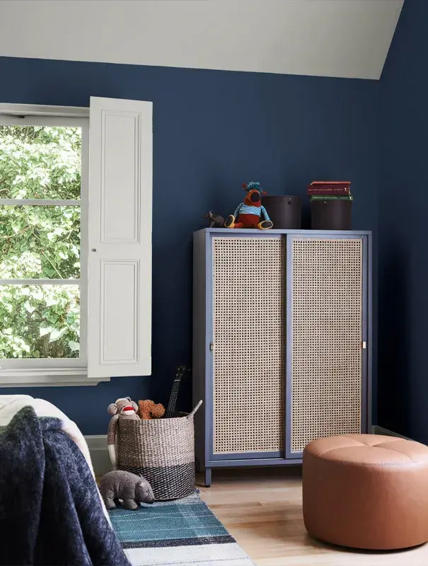 Blue child's bedroom with white shutters, vane wardrobe and brown leather pouf.