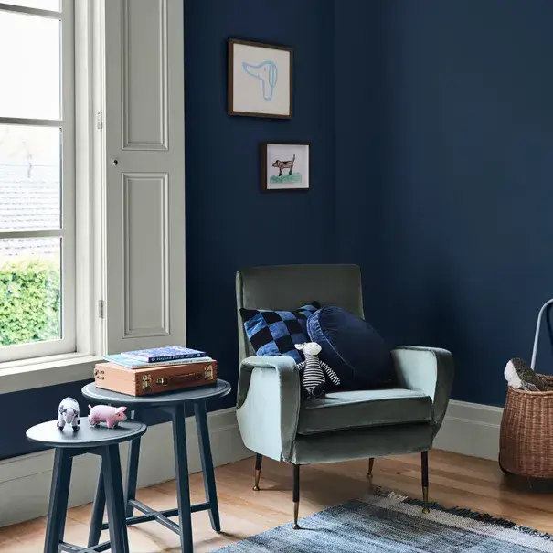 Navy child's room with white window frames, timber flooring, blue nesting tables and velvet armchair.