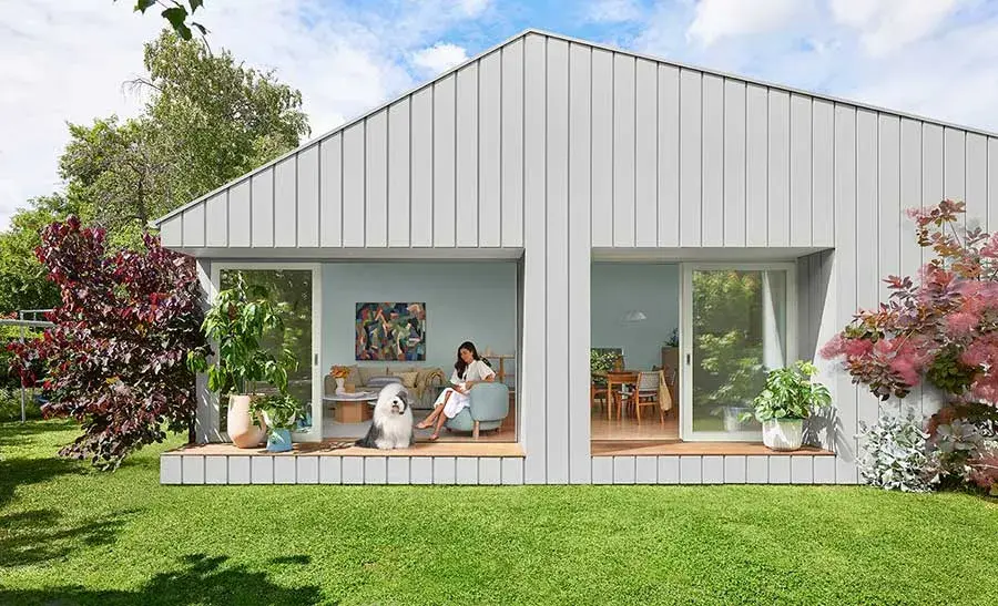 modern house with grey exterior opening onto lawn. A woman sits with a dulux old english sheep dog inside